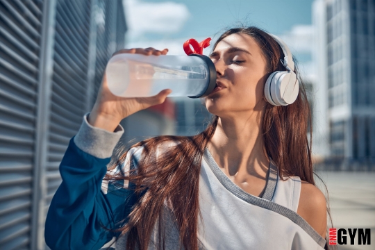 Female with headphones on drinking water to stay hydrated