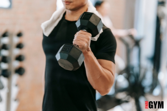 Male in gym holding dumbell doing bicep curl with towel over his shoulder