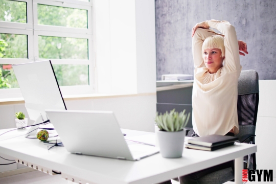 Middle aged female sitting stretching at desk doing at home workout