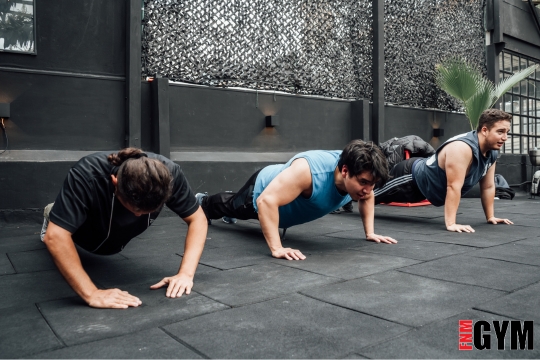 3 men performing pushups in a gym